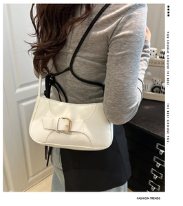 Detail of white glossy baguette bag featuring decorative belt straps and gold buckles