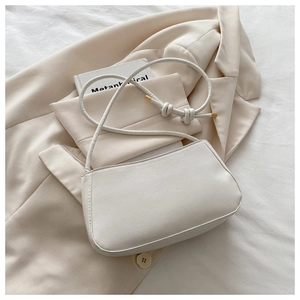 Close-up of white minimalist baguette bag featuring knot details on the slender shoulder strap
