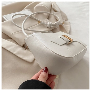 Close-up of white semi-circular shoulder bag featuring gold square buckle and knotted strap