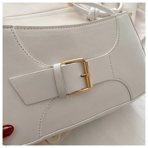 Detailed close-up of cream baguette bag with decorative gold buckle and leather texture