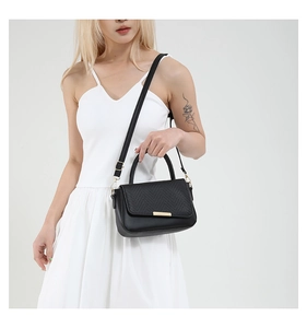 Detailed view of black leather handbag with woven flap and elegant gold metal buckle