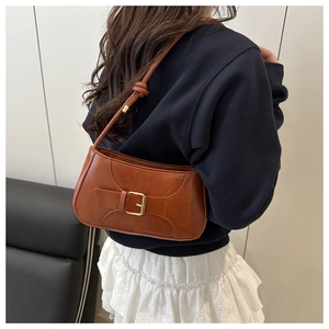 Detail of caramel brown baguette bag featuring decorative buckle and knot strap detail