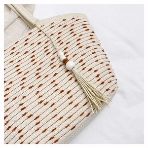 Detail of woven straw tote bag with brown tufted patterns and decorative wooden bead tassels