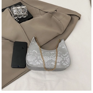 Detail of silver snake-pattern crescent bag with elegant gold chain strap on white surface