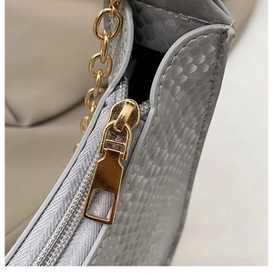 Close-up of snake skin texture with gold metal chain and zipper on a silver-grey handbag