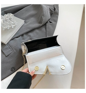 Détail de pochette argentée avec logo V doré, fermoir magnétique et bandoulière chaîne