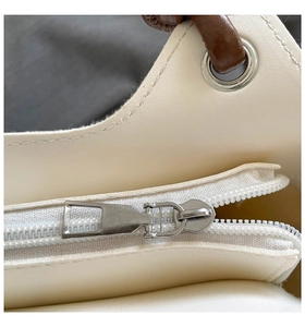 Detailed view of silver metal zipper and brown handles on minimalist white PU bucket bag