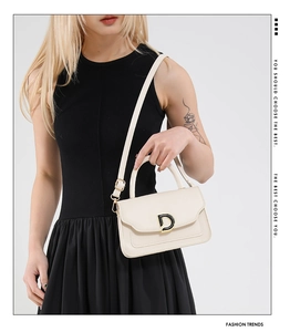 Detail of cream crossbody bag with gold D-buckle and adjustable strap on model