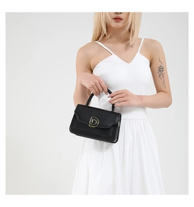Detail of minimalist black leather crossbody bag featuring a signature gold D-shaped buckle