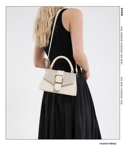 Detail of beige square handbag with sparkling sequins and gold buckle on a black dress