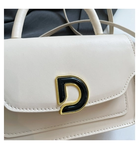 Close-up of cream leather bag featuring a large gold-toned metal letter D buckle