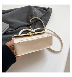 Close-up of a cream-colored structured handbag with a black and gold metal twist lock