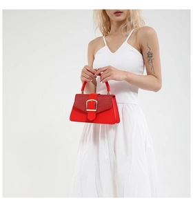 Detail of red square handbag with woven texture flap and golden buckle on white dress
