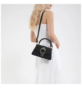 Detail of black crossbody bag with shimmering glitter flap and gold U-shaped buckle