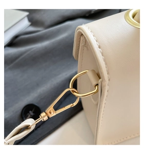 Detail of cream crossbody bag featuring golden D-ring hardware and neat leather stitching