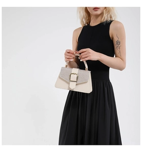 Detail view of cream handbag with silver sequins and gold buckle held by a model