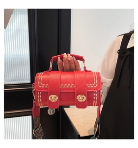 Detail of red cylinder bag with gold rivets, metal locks and patterned wide strap