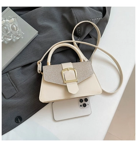 Close-up of cream square handbag with metallic texture flap and gold buckle detail