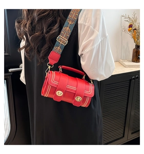 Detail of red cylindrical handbag featuring gold rivets and ethnic style woven strap