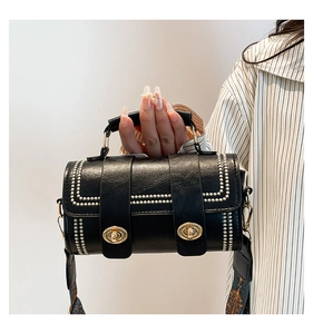 Detail of black textured leather cylinder bag with colorful woven strap and gold buckles