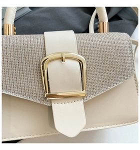 Detail of beige handbag featuring a sparkling woven flap and golden horseshoe buckle