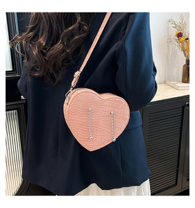Detail showing the pink heart-shaped crossbody bag with crocodile pattern and chain fringe