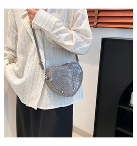 Detail of grey heart-shaped crossbody bag featuring crocodile texture and silver chain fringe