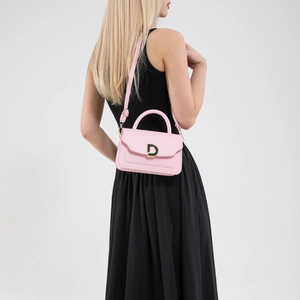 Pink minimalist crossbody bag with gold D-buckle shown on a model in a black dress