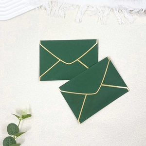 Close-up of deep green envelopes with gold foil edges on a white textured background