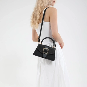 Fashionable black square handbag with glitter flap and gold buckle on a white outfit
