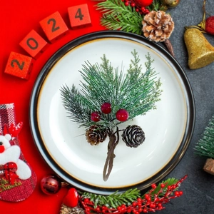 Servilletero navideño con bayas rojas y piñas en un plato de cerámica blanca