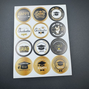 Close-up of black and gold graduation party stickers with graduation cap and scroll designs