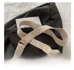 Close-up of beige straw bag with geometric shoulder strap and gold metal letter M decoration