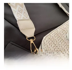 Close-up of golden metal hooks and jacquard strap on a beige woven shoulder bag