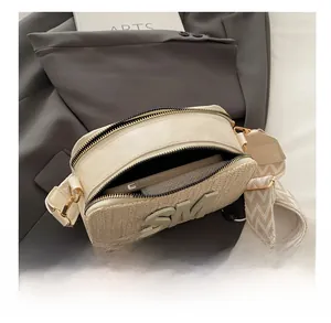 Detail of cream woven crossbody bag with metal zippers showing inner phone storage capacity