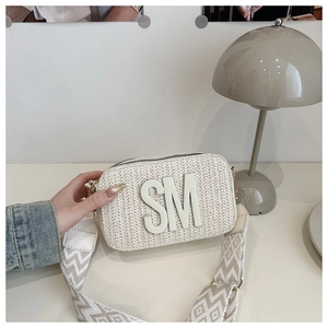 Detail of cream woven crossbody bag featuring SM logo and wide wavy shoulder strap