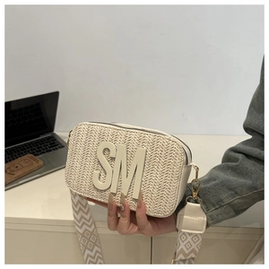 Detail of straw woven crossbody bag with bold SM logo and geometric strap pattern