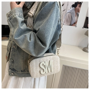 Detail of woven straw crossbody bag featuring a bold SM logo and wide jacquard strap