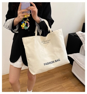 Detailed view of cream canvas tote bag featuring black Fashion Bag text on the front