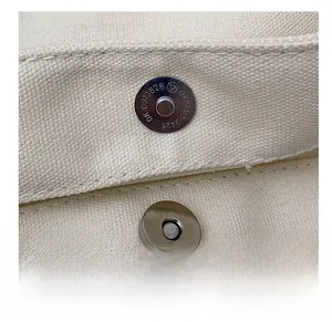 Close-up of magnetic metal snap fastener on cream canvas tote bag with serial engraving