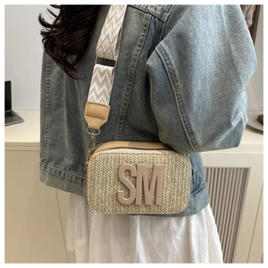 Detailed macro view of straw woven crossbody bag with SM lettering and geometric strap