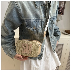 Close-up of woven crossbody bag with large SM logo and adjustable fabric strap