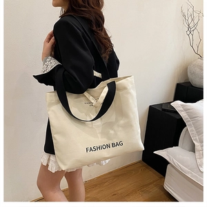 Detail of spacious canvas tote bag with black straps and fashion lettering on white fabric