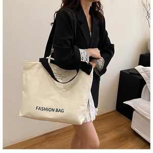 Detail of off-white canvas tote bag featuring black wide strap and fashion lettering print