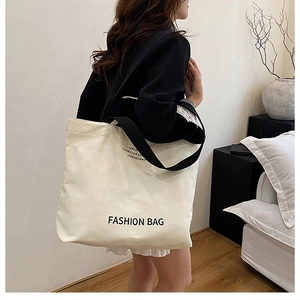 Detail of a beige canvas tote bag with black straps and fashion lettering on the side