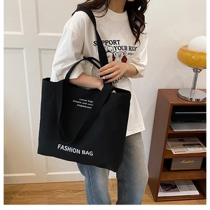 Detail of a black canvas tote bag with white lettering and long shoulder straps
