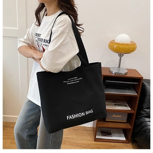 Close-up of a large black canvas tote bag with white slogan and comfortable straps