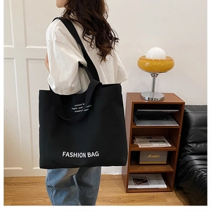 Detail of black canvas tote bag featuring white Fashion Bag print in a lifestyle setting