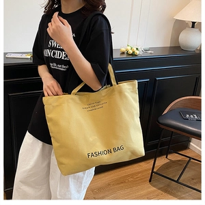 Detail of yellow canvas tote bag with fashion lettering worn by a model in home setting