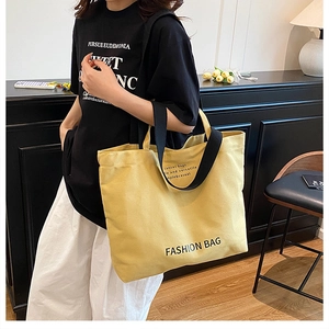 Yellow canvas tote bag with black straps worn by model in a minimalist home setting